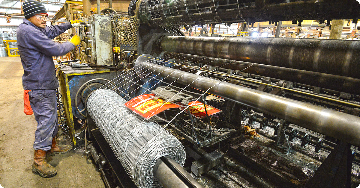 A man in a fence production facility winds up a roll of fencing.