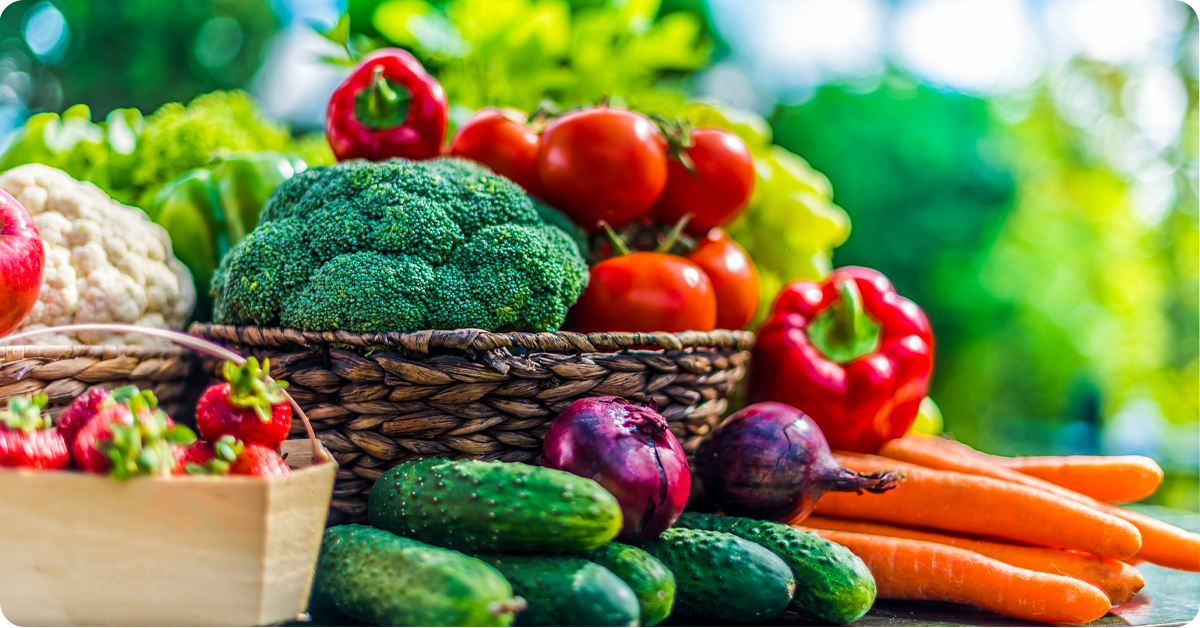 A wicker basket filled with fresh garden produce like tomatoes, peppers, carrots, onions, and more.