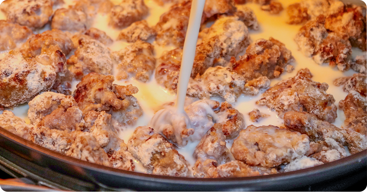Buttermilk being poured onto a hot skillet of sausage.
