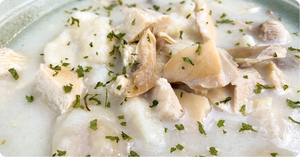 A bowl of chicken and dumplings in a white mushroom sauce with green parsley.