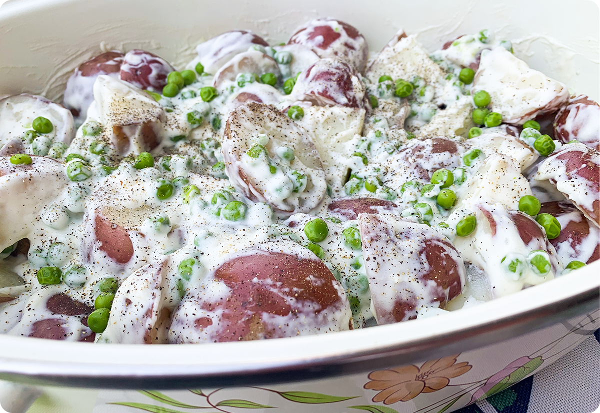 A bowl of quartered red potatoes and peas in a white cream.