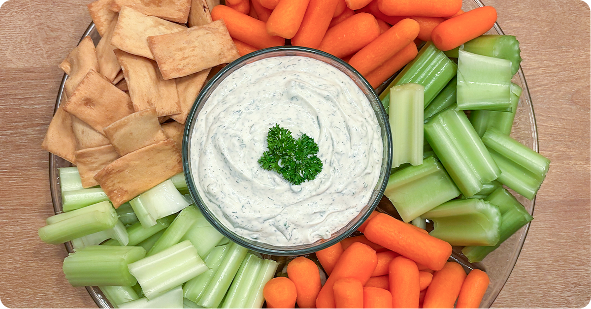 A glass tray with Jones' Beau Monde Vegetable Dip and carrots, celery, and crackers.